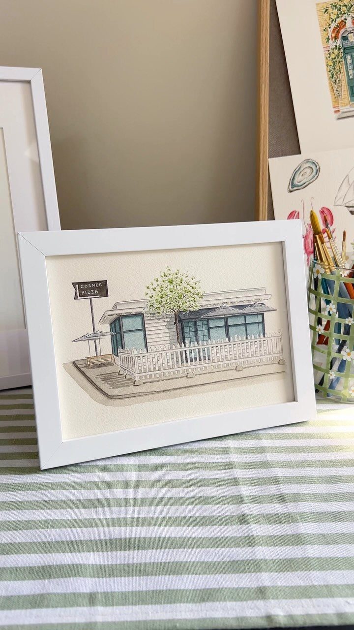 Watercolor illustration of a building in a white frame on striped fabric.