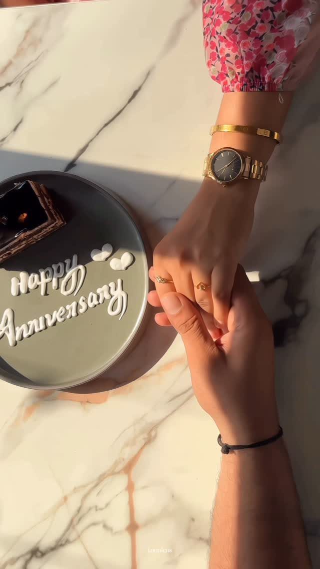 Couple holding hands next to a chocolate dessert with Happy Anniversary icing
