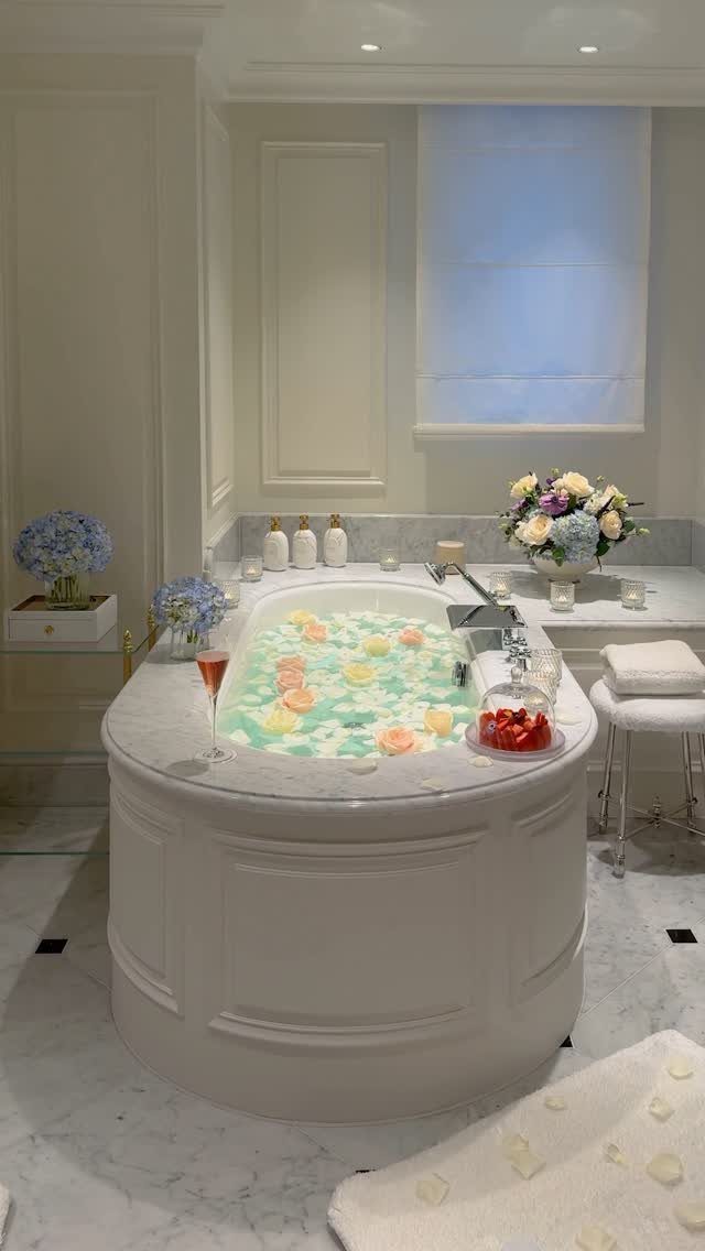 White bathtub with floating petals, champagne, and strawberries in a luxury bathroom.