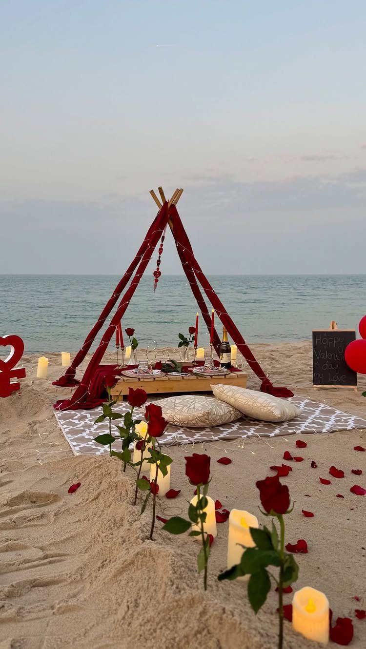 Romantic beach picnic setup with a red teepee, candles, and red roses.