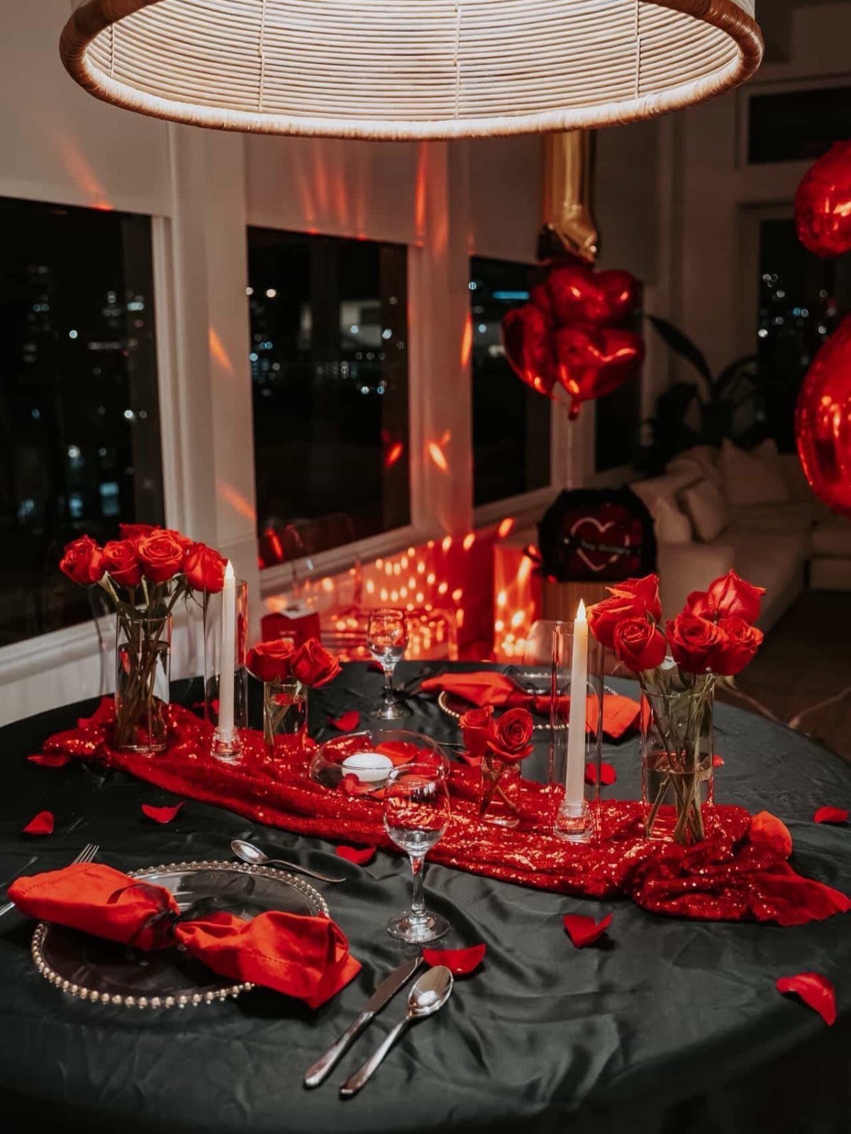 Romantic dinner table with red roses, candles, and sequins for an anniversary celebration.