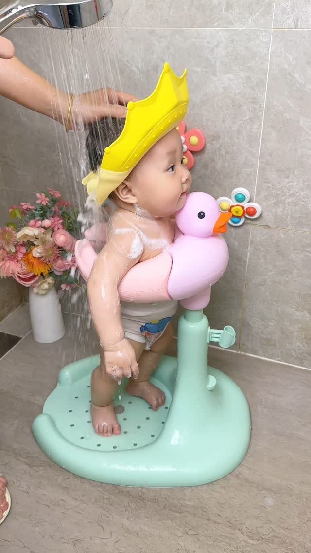 Baby in a pink duck bath seat wearing a yellow crown under a shower