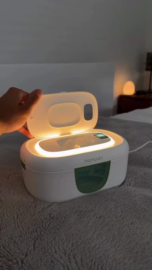 White and green baby bottle warmer glowing with light on a grey blanket