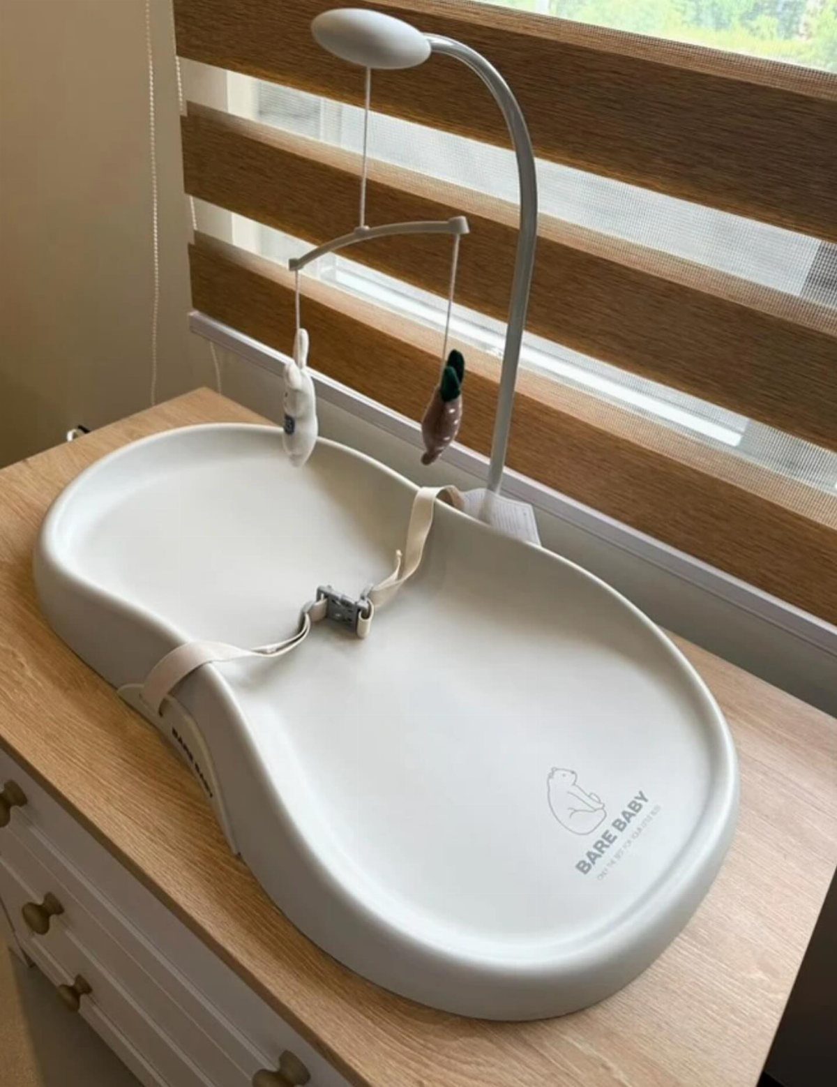 White baby changing pad on a wooden dresser with a toy mobile above.