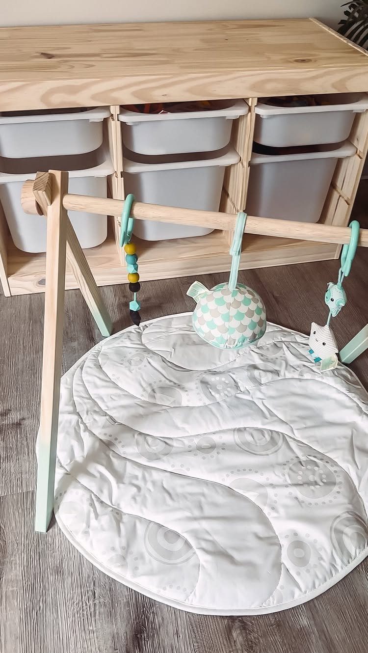 Wooden baby play gym with white padded mat and hanging colorful toys.