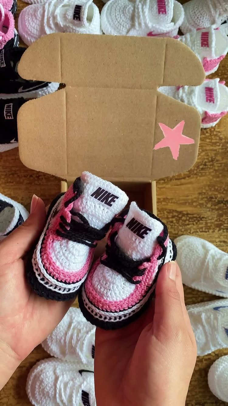 Crocheted baby sneakers in white and pink held by two hands.