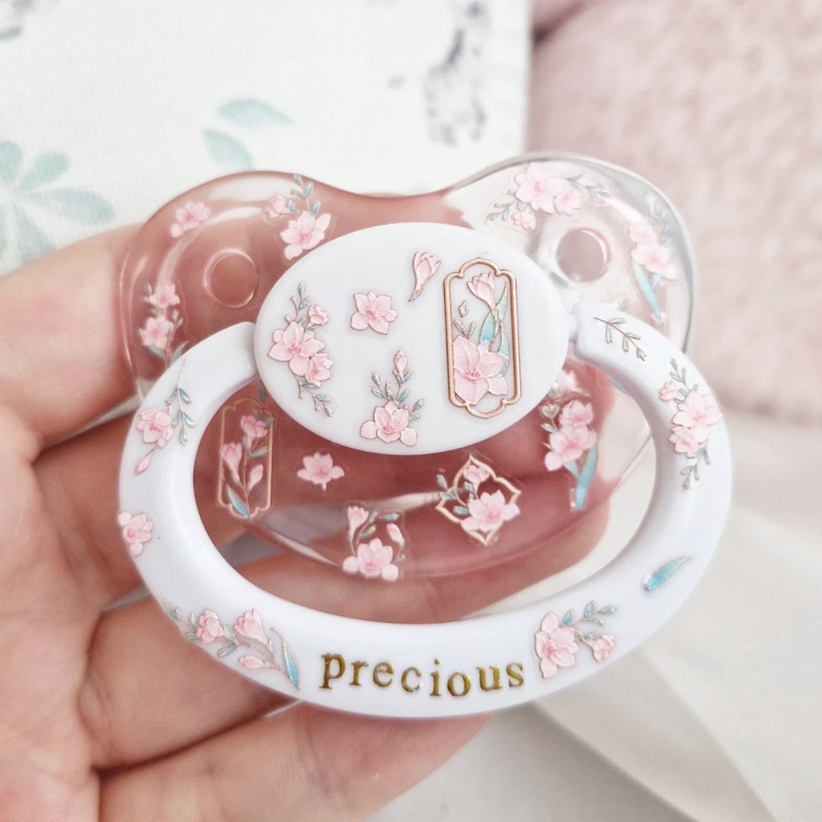 White and clear baby pacifier with pink cherry blossoms and gold Precious text.