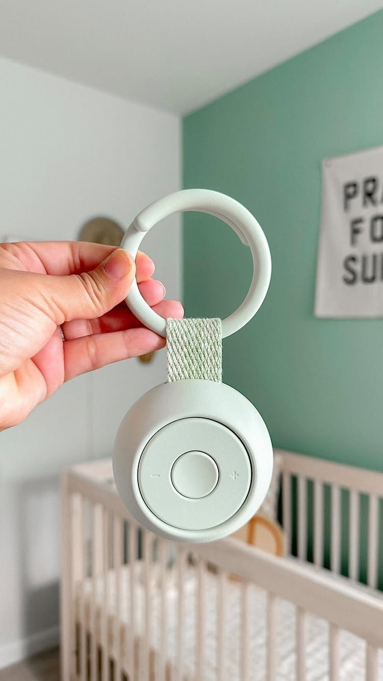Mint-green portable baby sound machine held in front of a white baby crib.