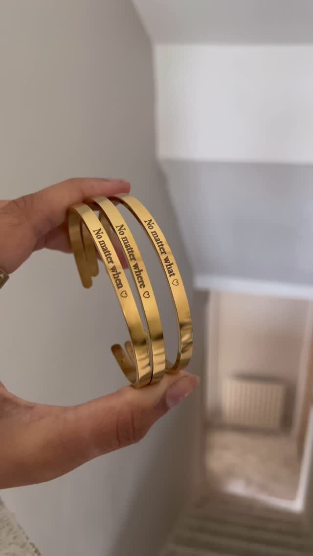 Three gold cuff bracelets with engraved romantic messages held in a person's hand.