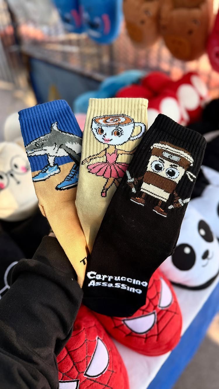 Three pairs of novelty socks featuring coffee and shark characters held by a person.