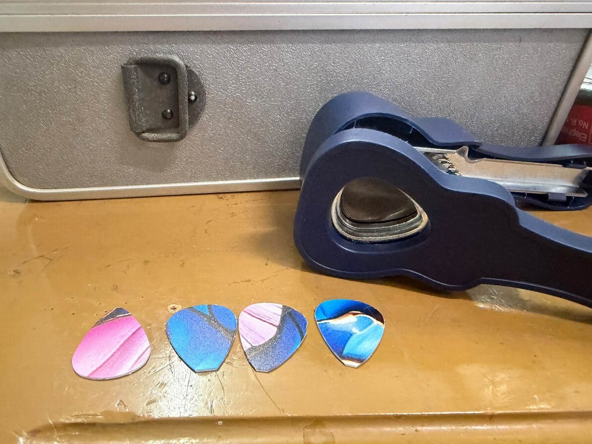 Blue guitar pick punch tool with four colorful custom guitar picks on a table