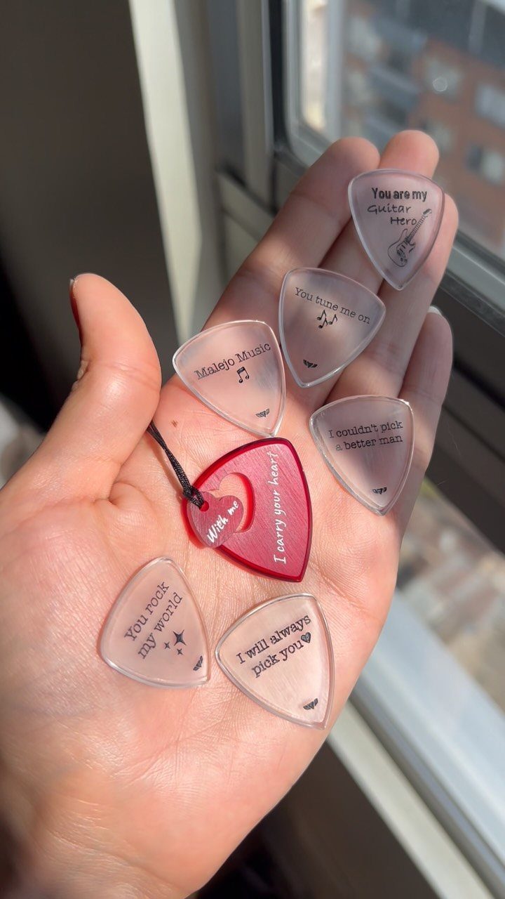 Hand holding several personalized translucent guitar picks with romantic messages and musical notes.