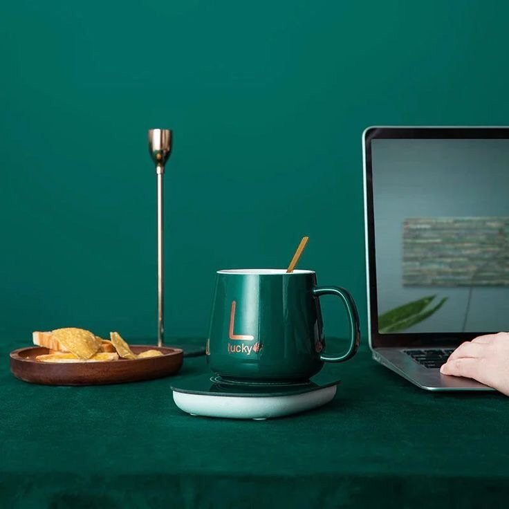 Green personalized mug on a warming coaster next to a laptop and snacks.