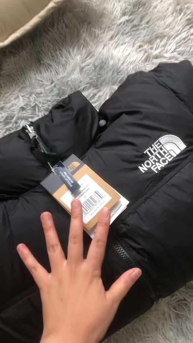 Black puffer jacket with tags resting on a white shaggy rug.