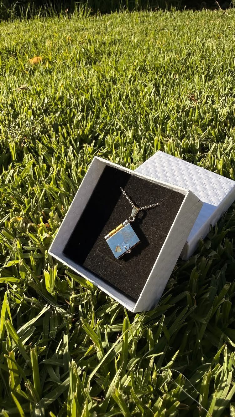Blue rectangular pendant necklace in a white jewelry box on green grass