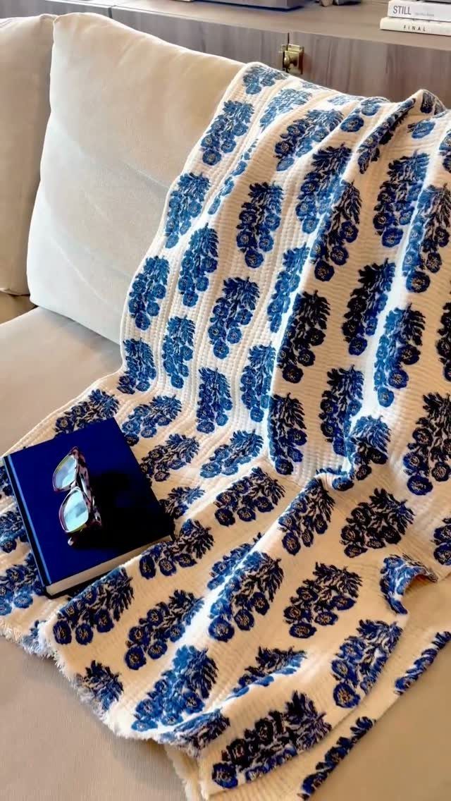 Blue floral patterned throw blanket on a white sofa with a book and glasses