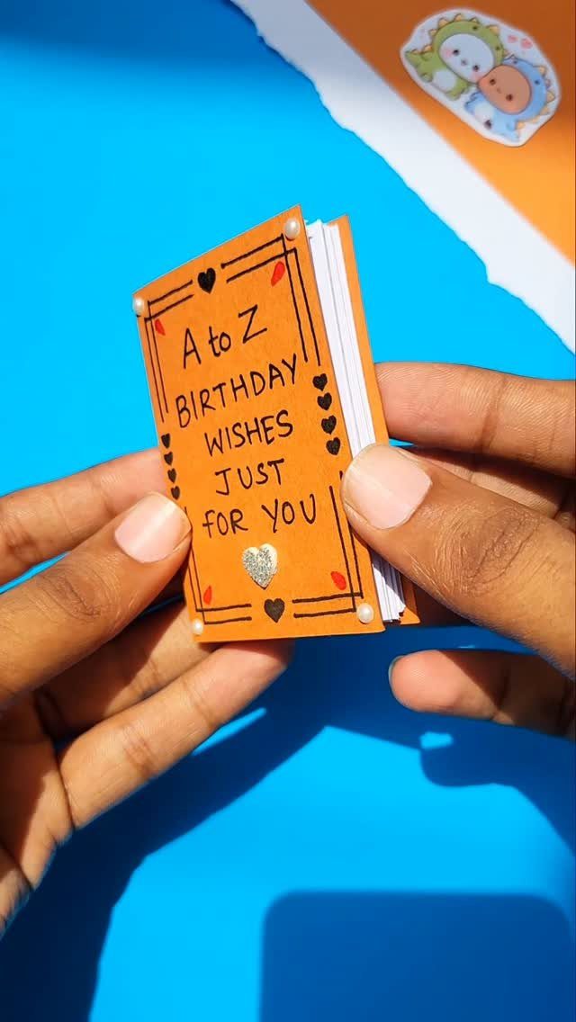 Handmade orange birthday wishes notebook held by two hands against a blue background