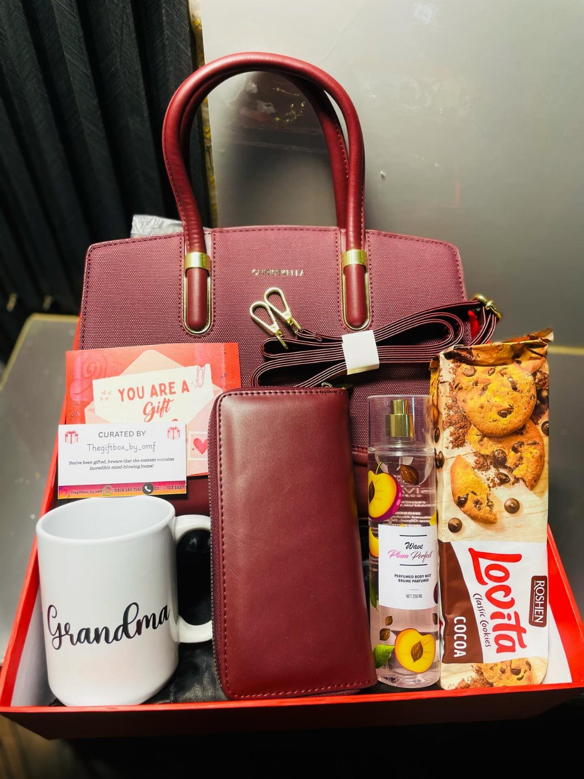 Red gift tray with handbag, wallet, Grandma mug, perfume, and cookies.