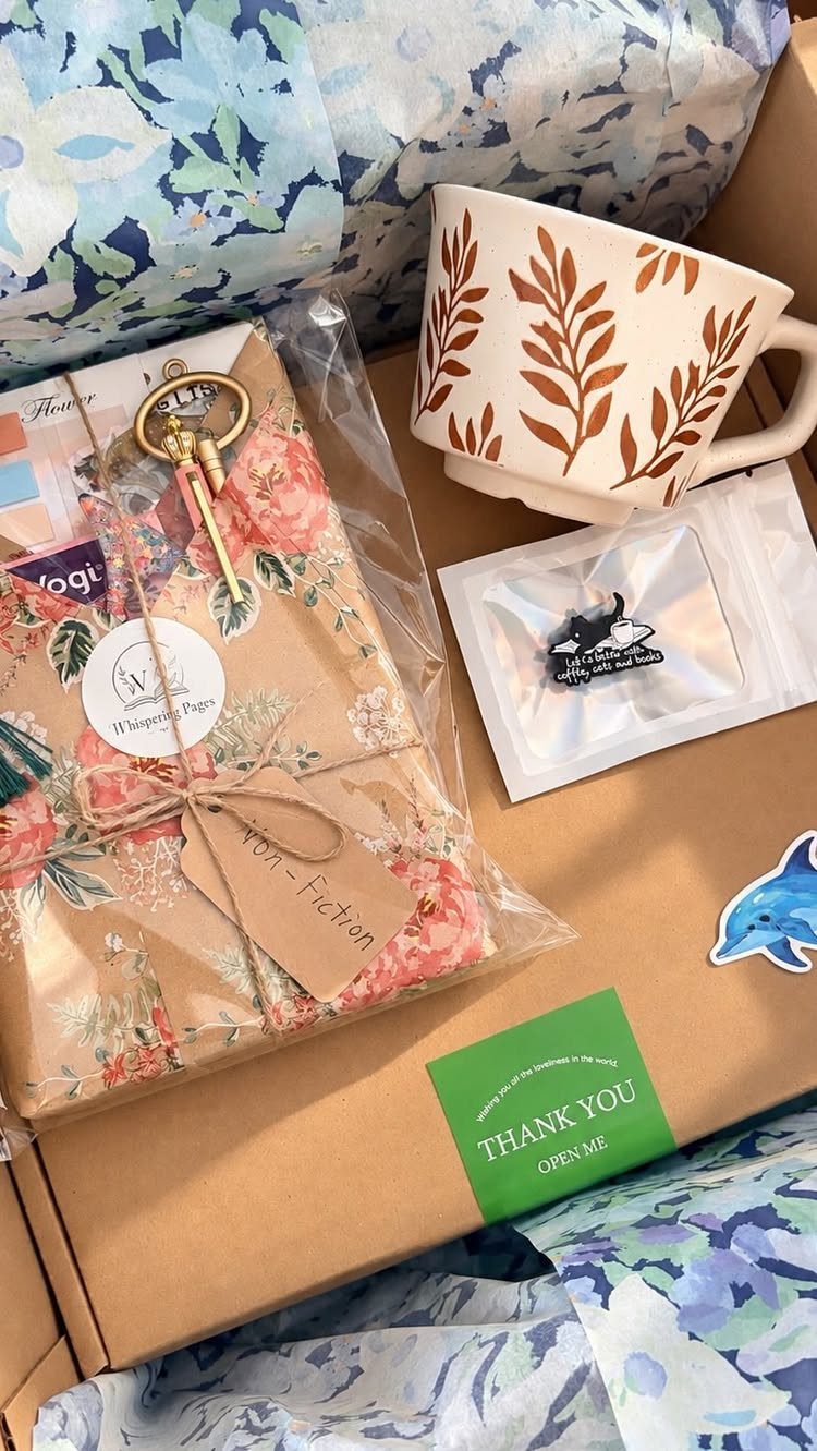 Gift box with a leaf-patterned mug, floral wrapped book, and thank you card.