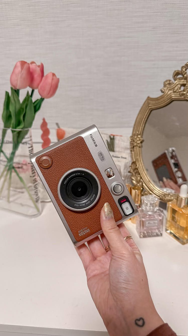 Brown and silver instant film camera held in a hand near pink tulips.