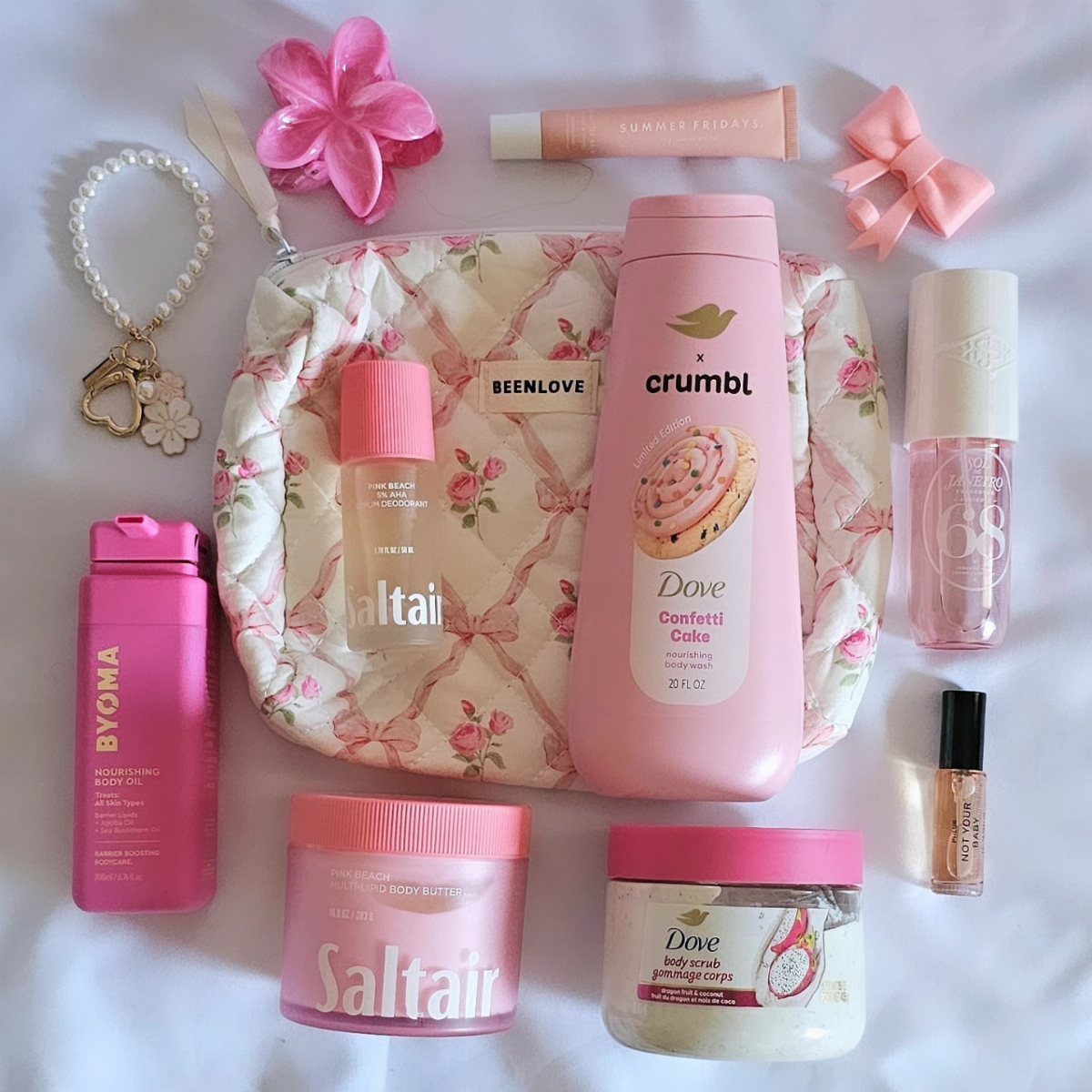 Pink beauty products and skincare items arranged around a floral quilted makeup bag.