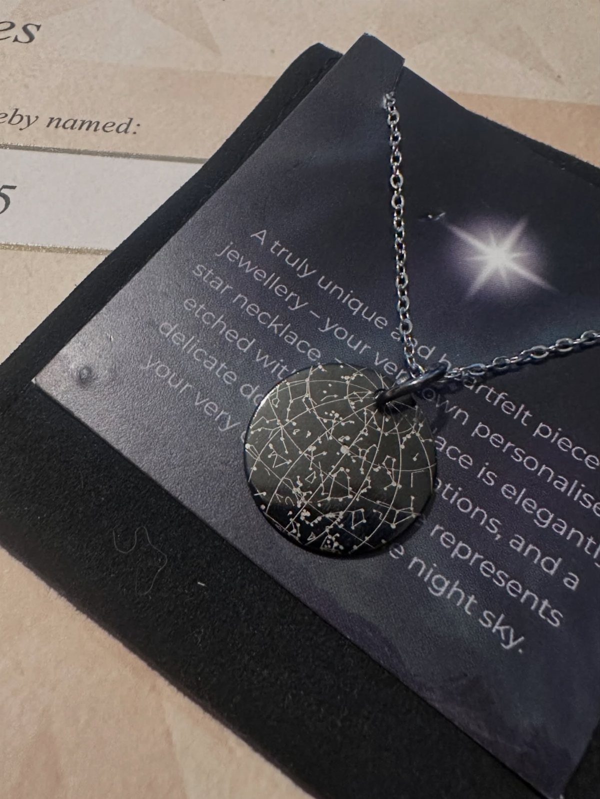 Silver star map constellation necklace resting on a black descriptive gift card.