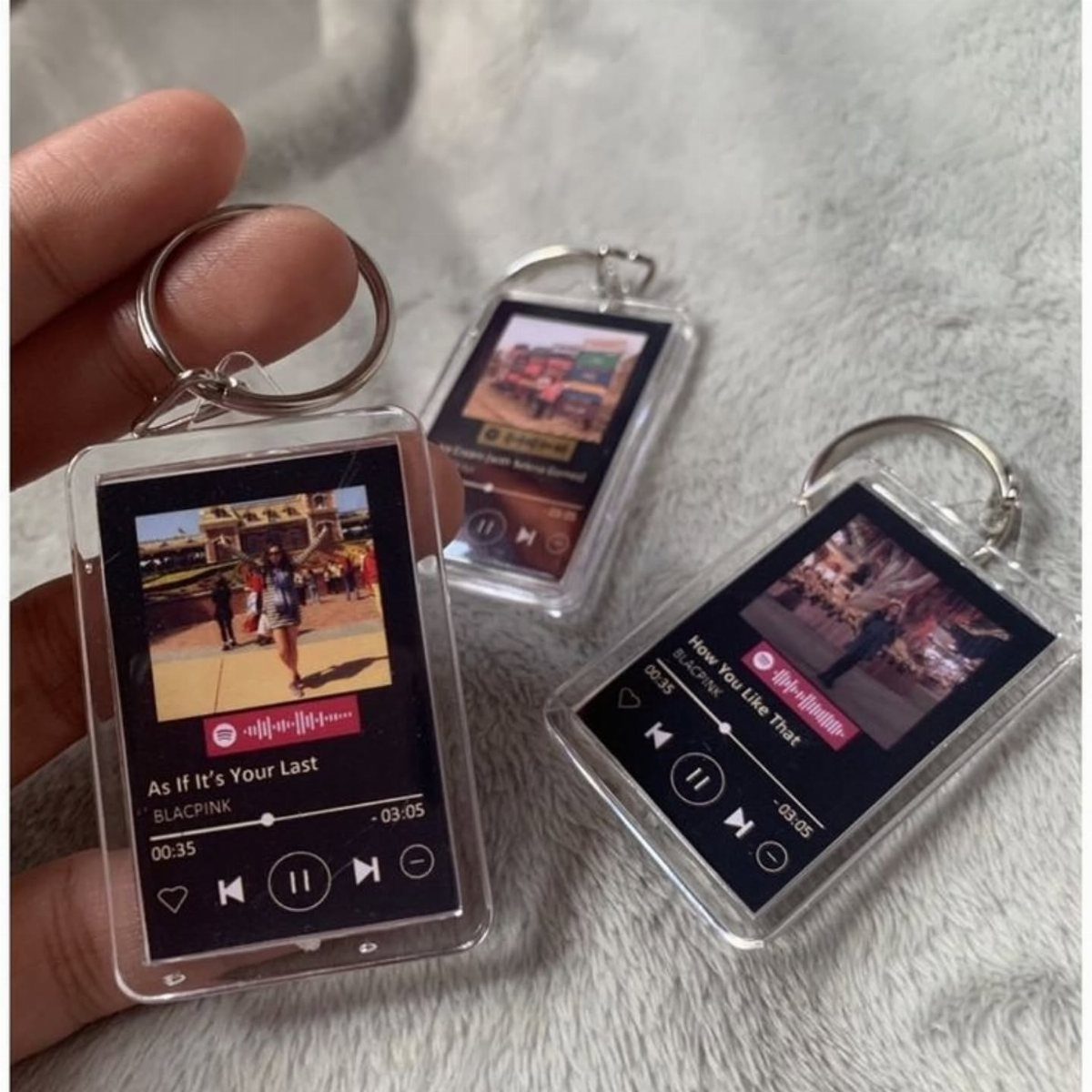 Acrylic music player keychains with custom photos and song titles on white fur.