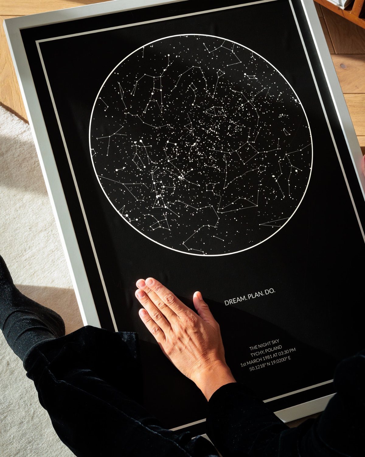 Framed black star map with white constellations and text held by a person.