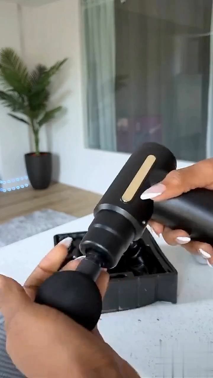 Black handheld massage gun with round attachment held over its storage case.