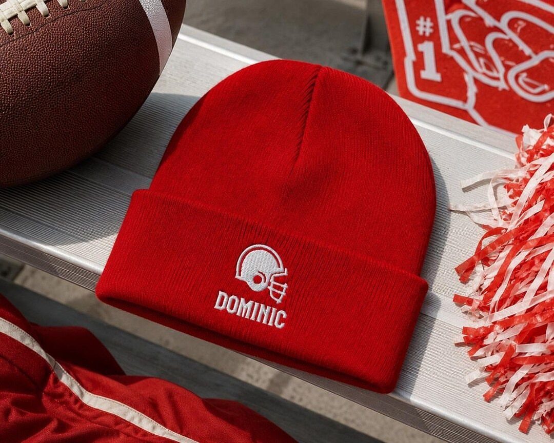 Red knit beanie with white football helmet and name Dominic on white bench