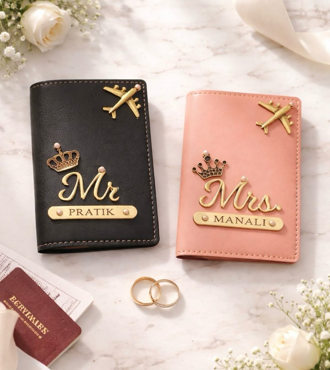 Black and pink personalized passport holders with gold airplane charms on marble surface