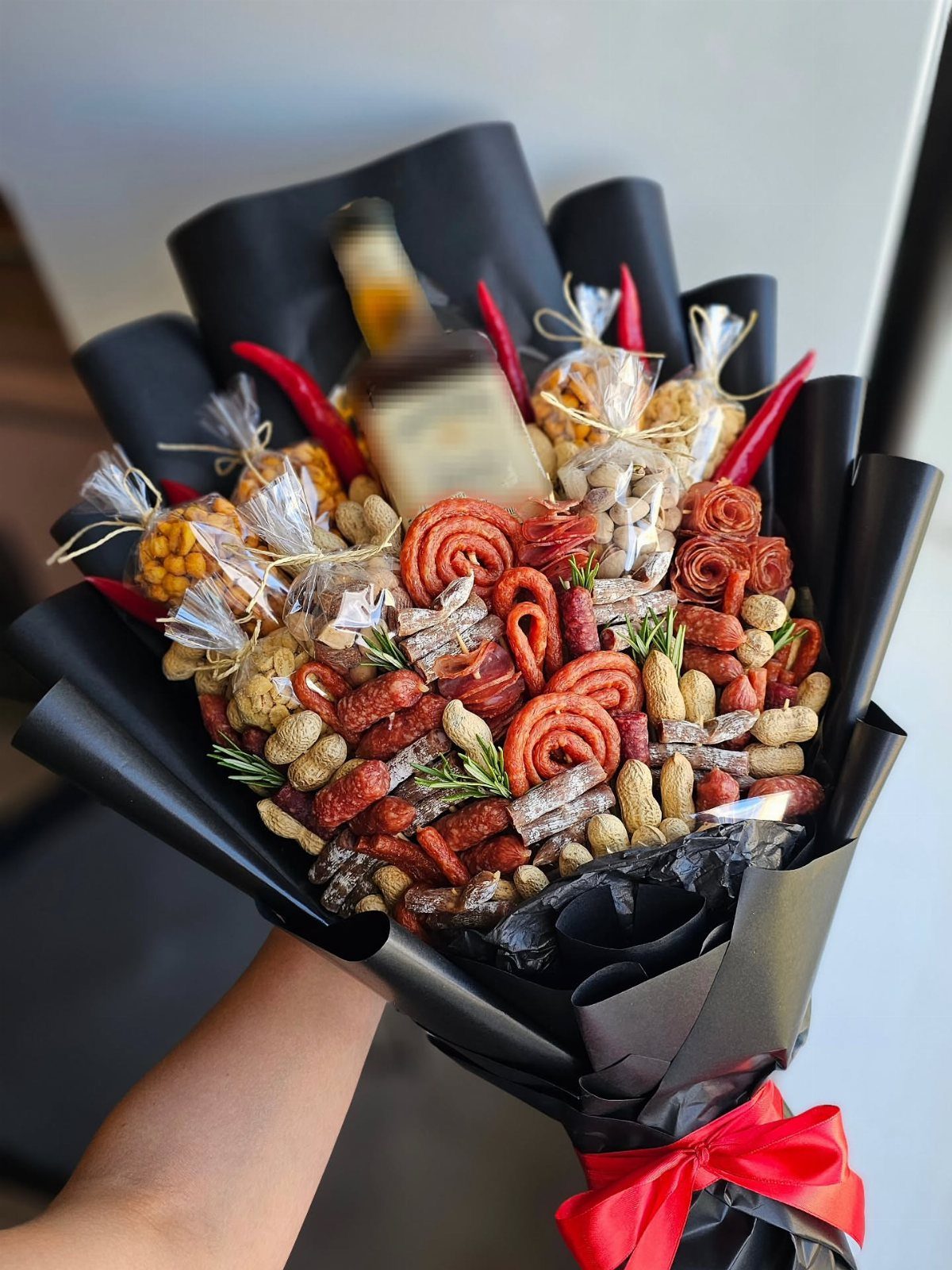 Savory snack bouquet with liquor bottle, pretzels, and nuts wrapped in black paper.