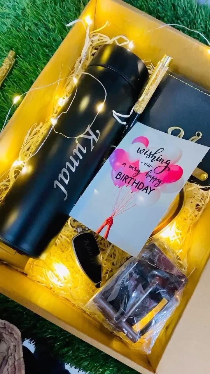 Gift box with personalized black water bottle, wallet, and birthday card on grass.