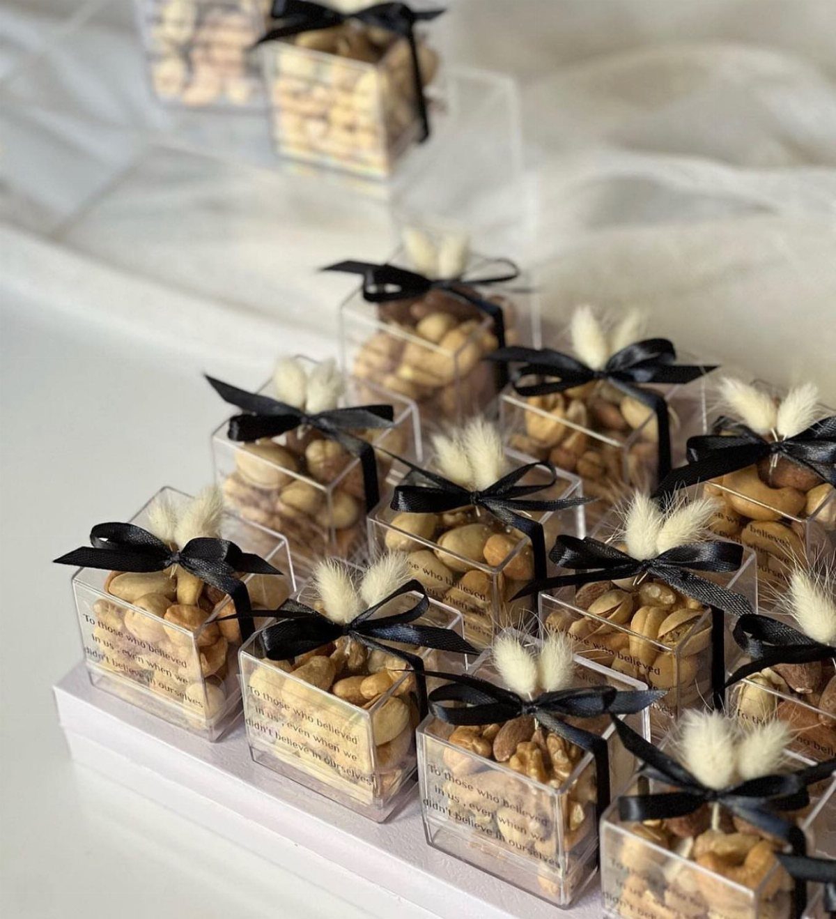 Candied nuts in clear square gift boxes tied with black ribbons and white florals.