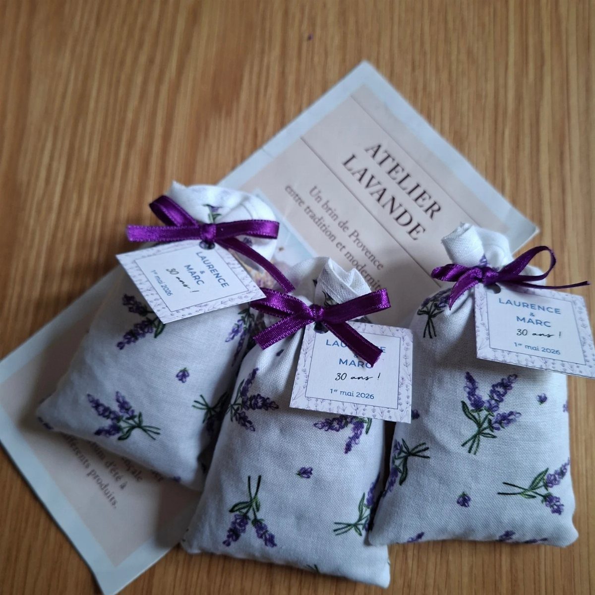 Three lavender printed fabric sachets tied with purple ribbons and personalized gift tags.