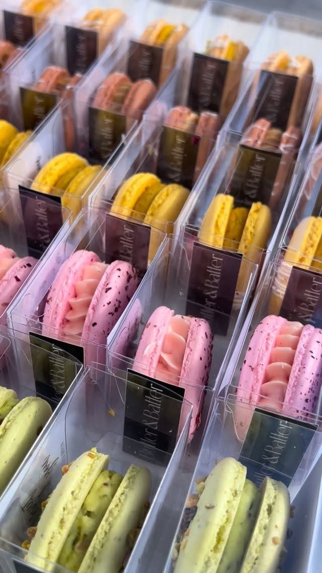 Colorful macarons in clear plastic treat boxes with small black labels arranged in rows.