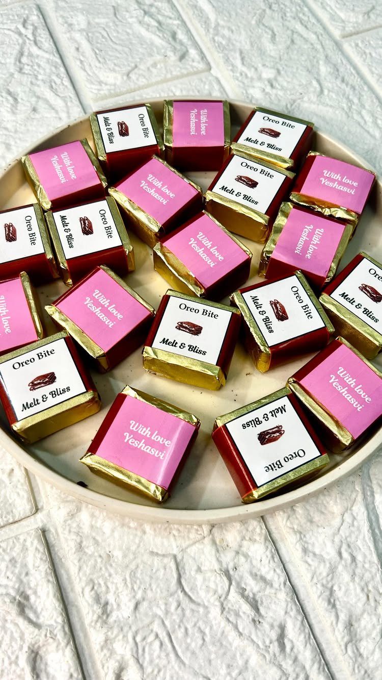 Square chocolates wrapped in gold foil with pink and white custom stickers on a plate