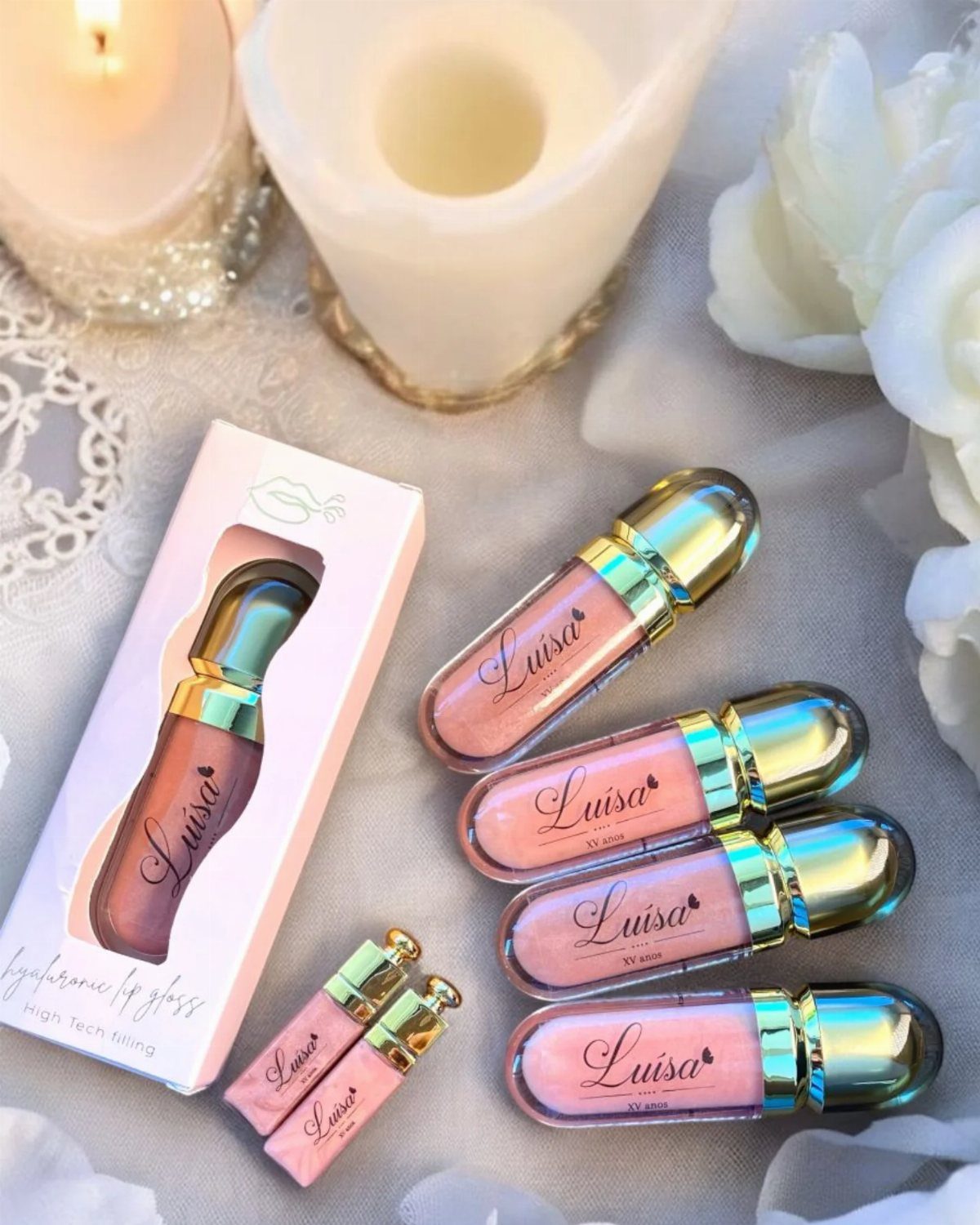 Lip gloss tubes with personalized names and gold caps on white fabric.