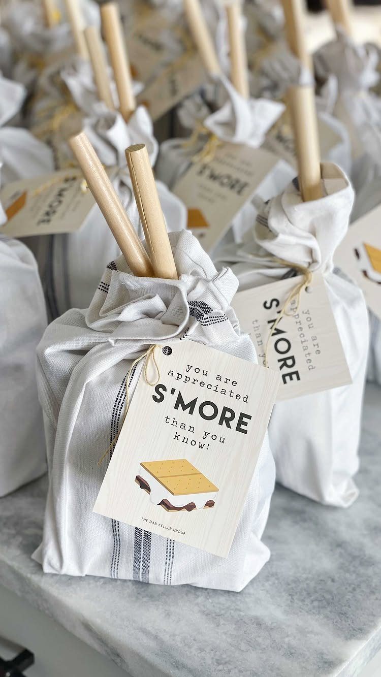 White fabric drawstring bags containing s'mores kits with wooden sticks and punny tags.