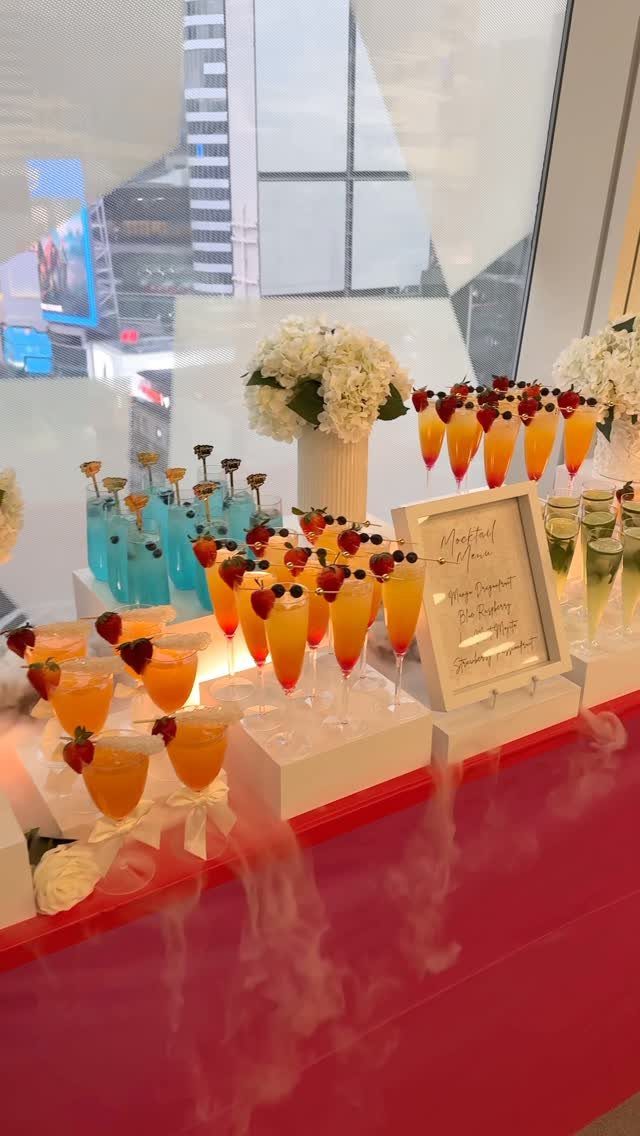 Colorful garnished drinks and cocktails arranged on a red counter with white flowers.