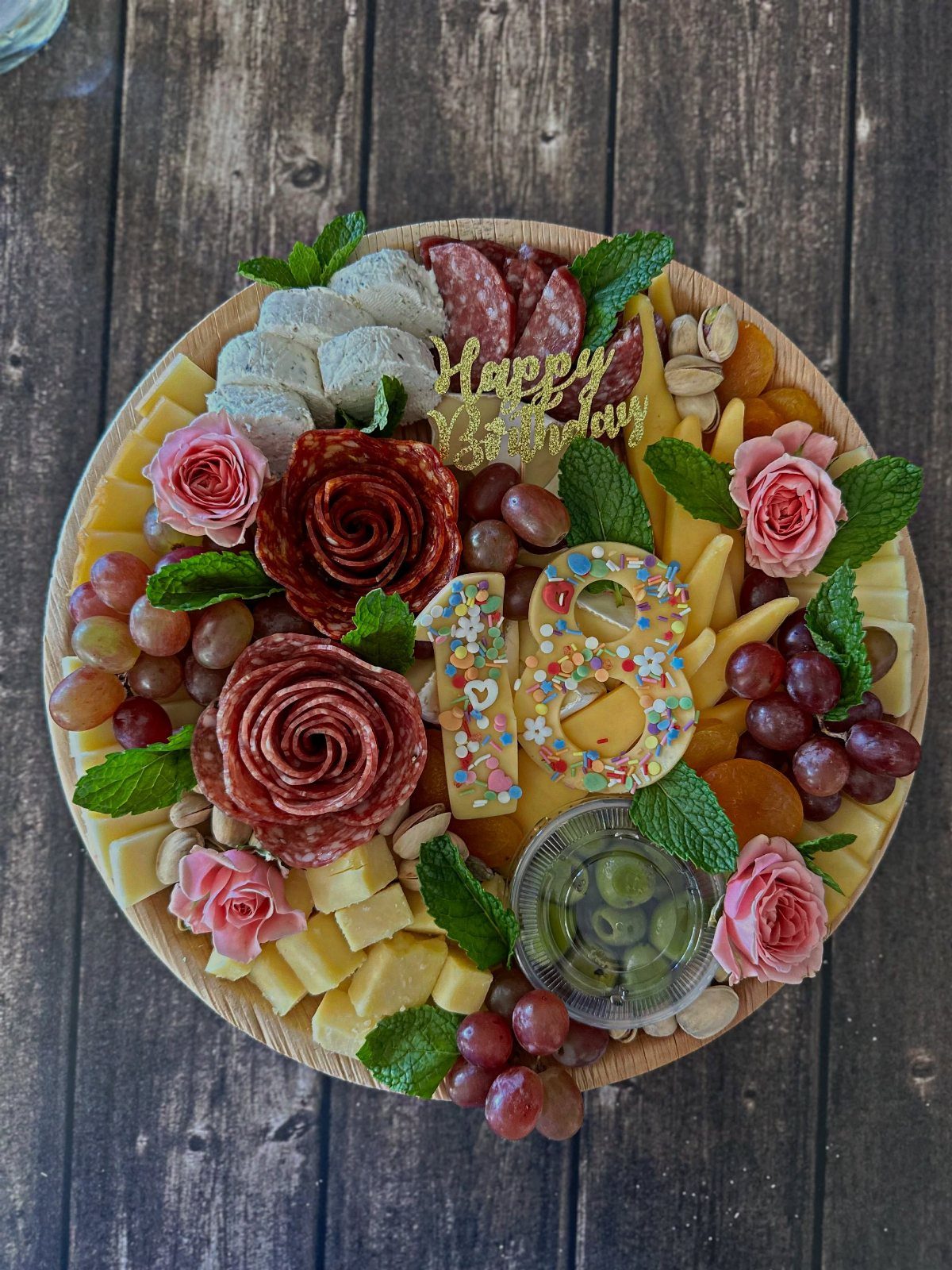 Charcuterie board with meats, cheeses, and fruits featuring 18th birthday cake toppers.