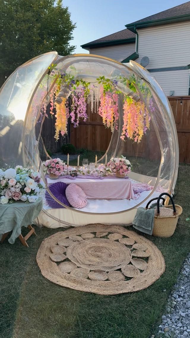 Clear bubble tent with pink floral decorations and a low table on grass