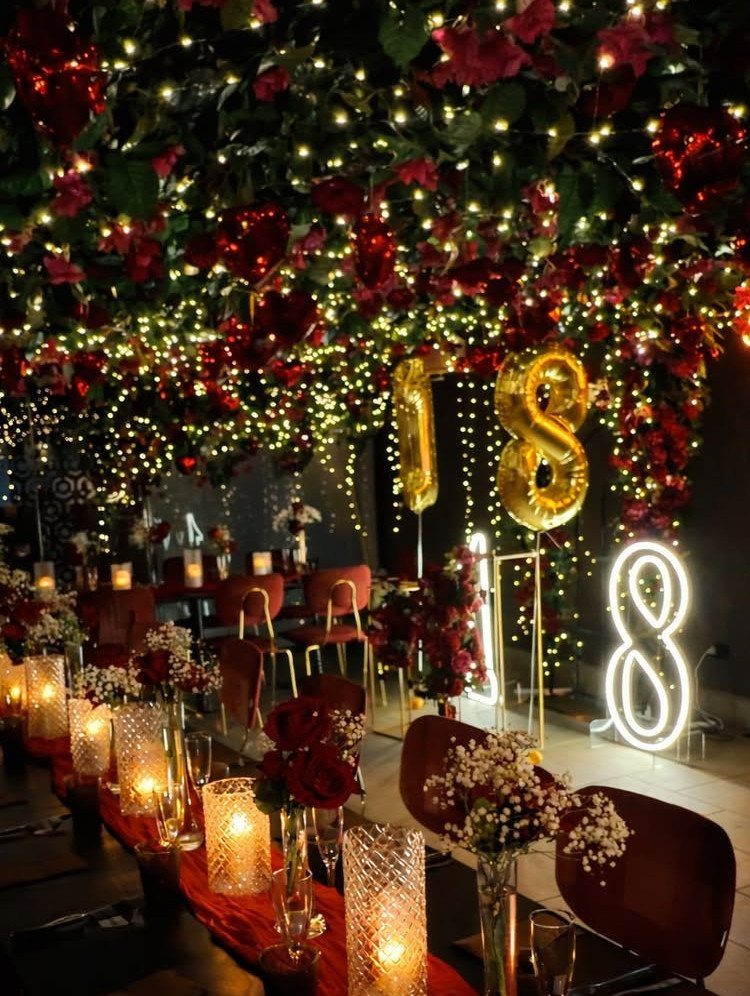 Dinner table with red roses and candles under fairy lights with 18 balloons.