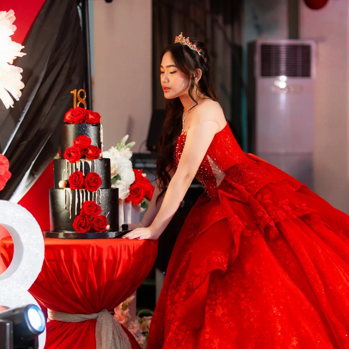 Young woman in red ballgown standing by a black 18th birthday cake