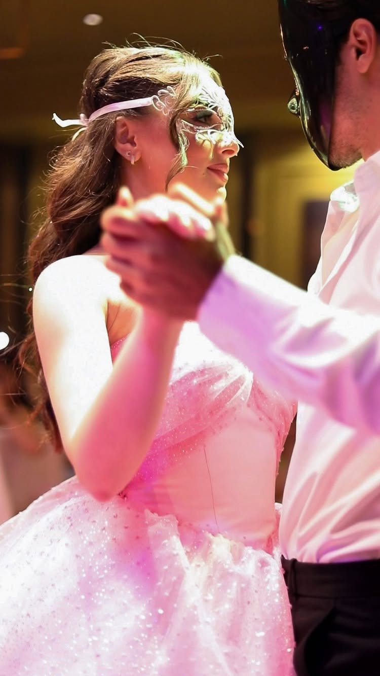 Young woman in pink gown and silver mask dancing with a masked man.