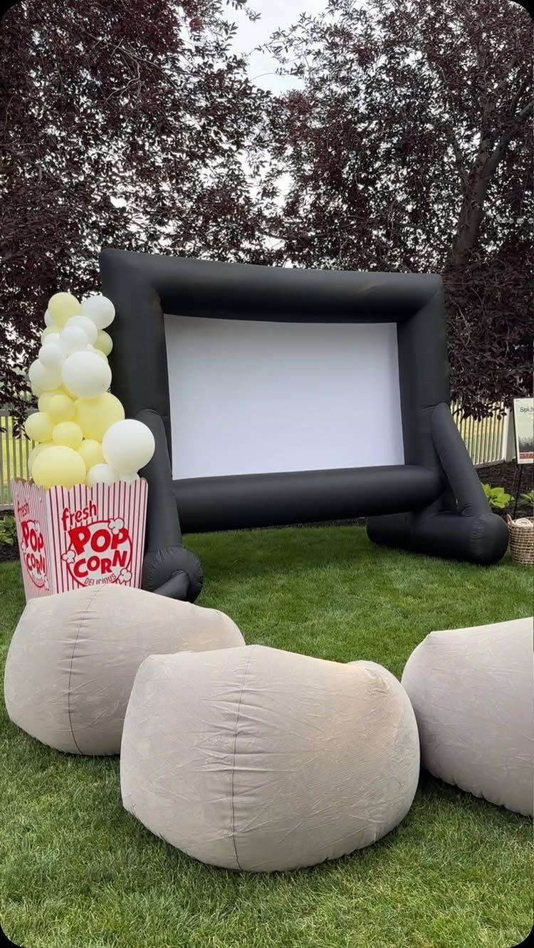 Inflatable movie screen and bean bag chairs on a lawn with popcorn balloons.