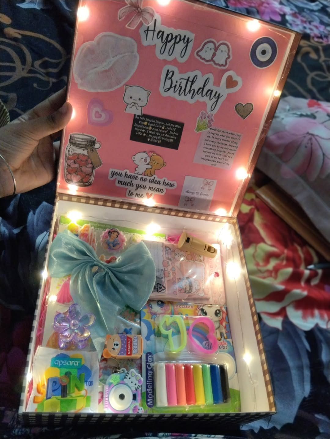 Open birthday gift box filled with stationery, modeling clay, and LED string lights.