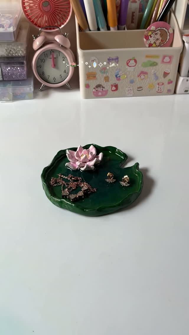 Green leaf-shaped trinket dish with a pink lotus flower holding gold jewelry.