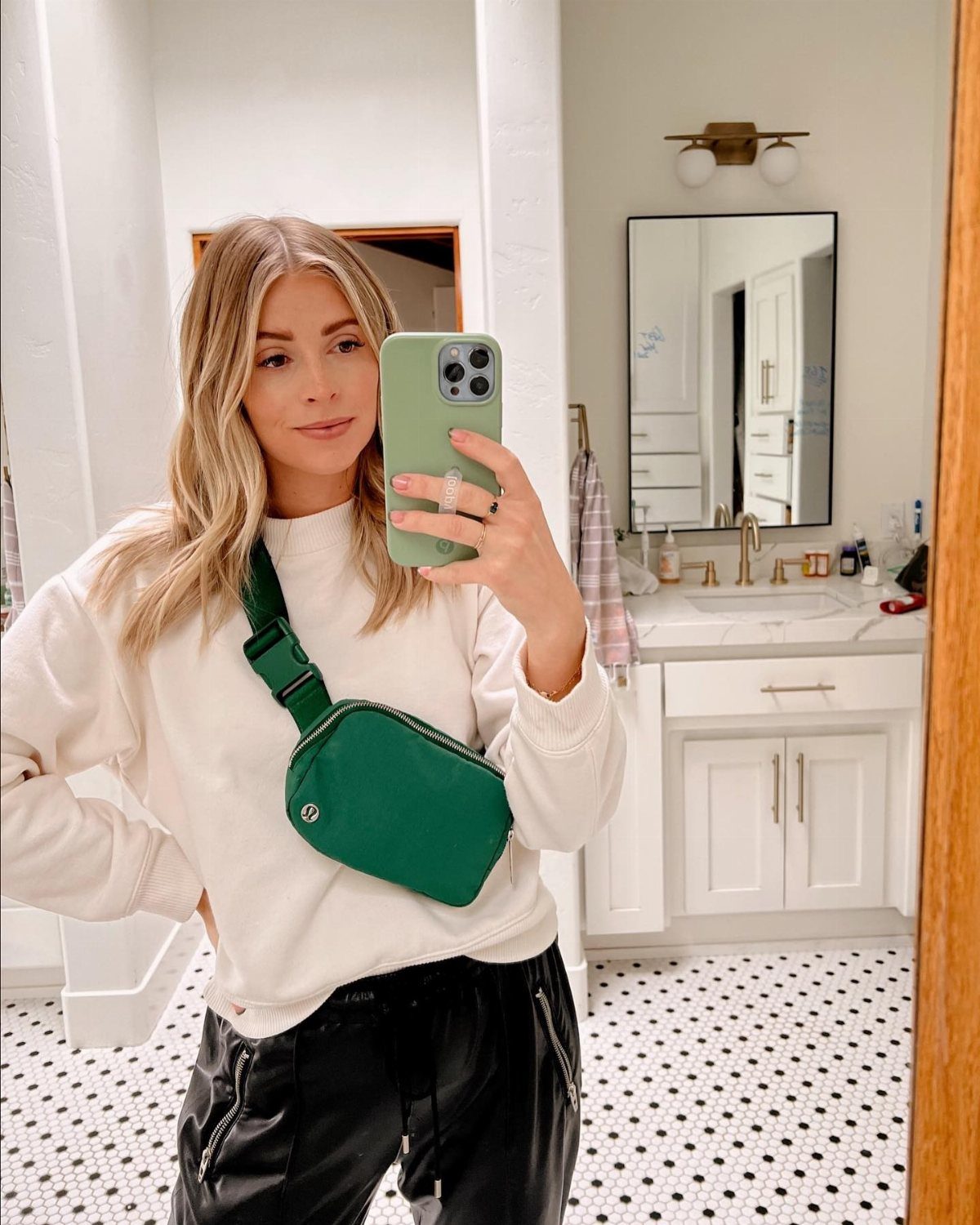 Woman wearing a green lululemon belt bag crossbody in a bathroom mirror selfie.