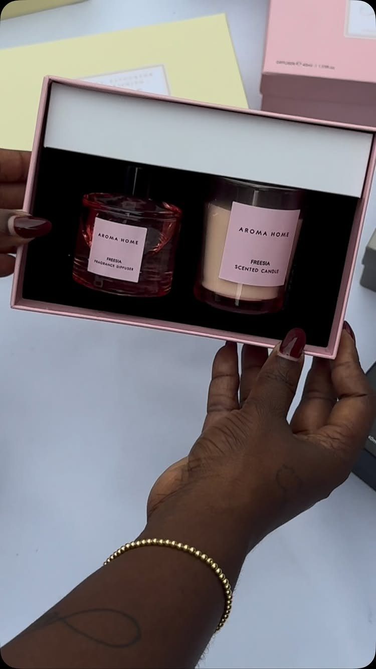 Two scented candles in a pink gift box held by a person's hands.